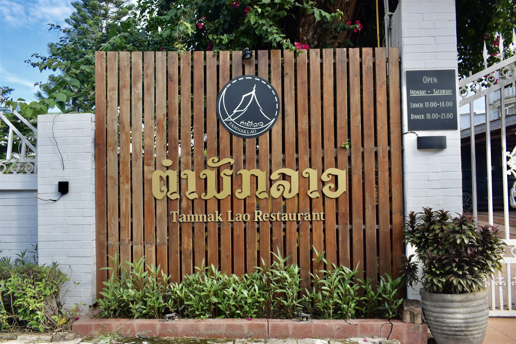Tamnak Lao Restaurant entrance signage on Singha Road, with opening hours
